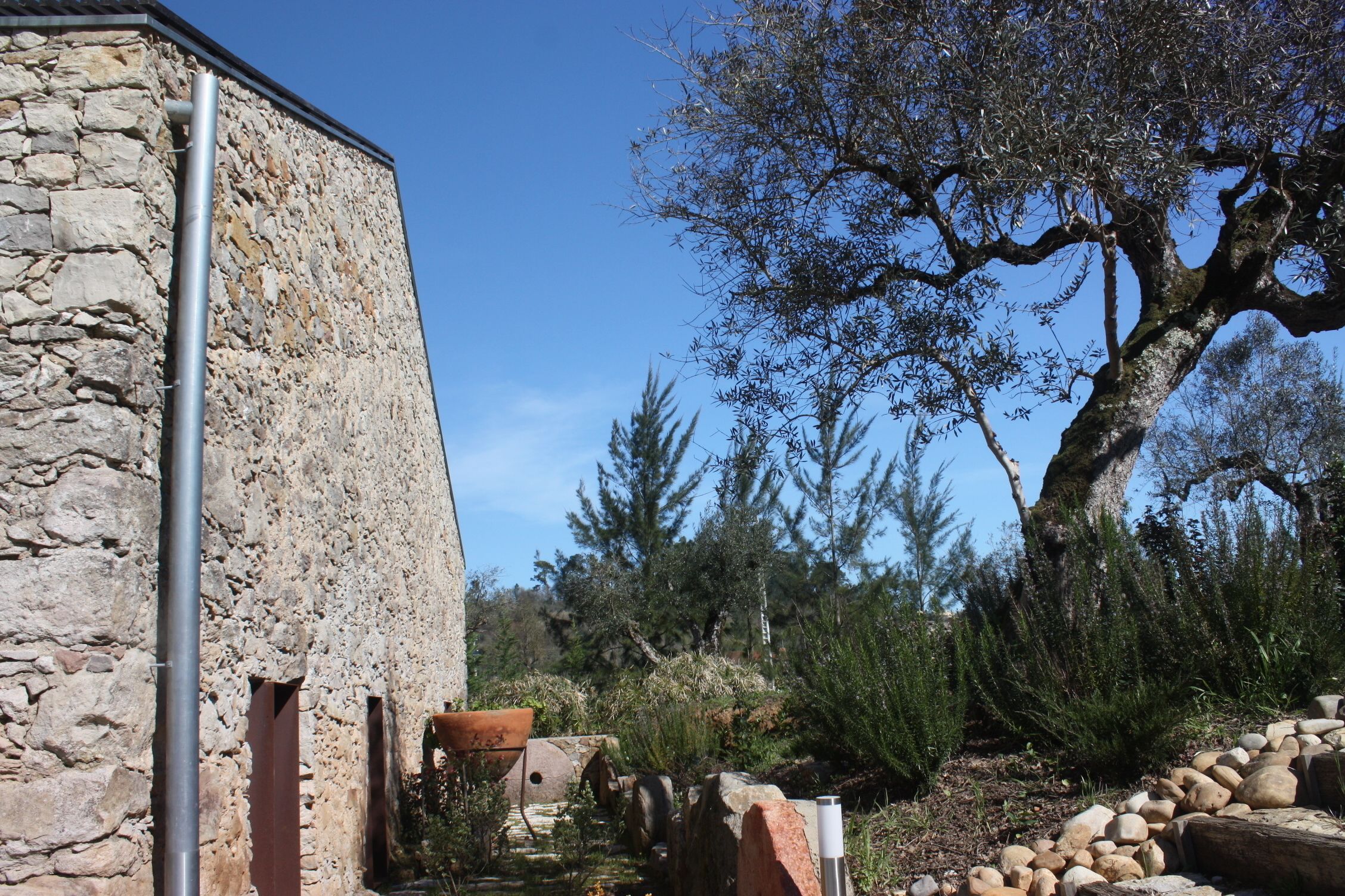 Edifici de pedra amb un tub metàl·lic, envoltat de roques i arbres.