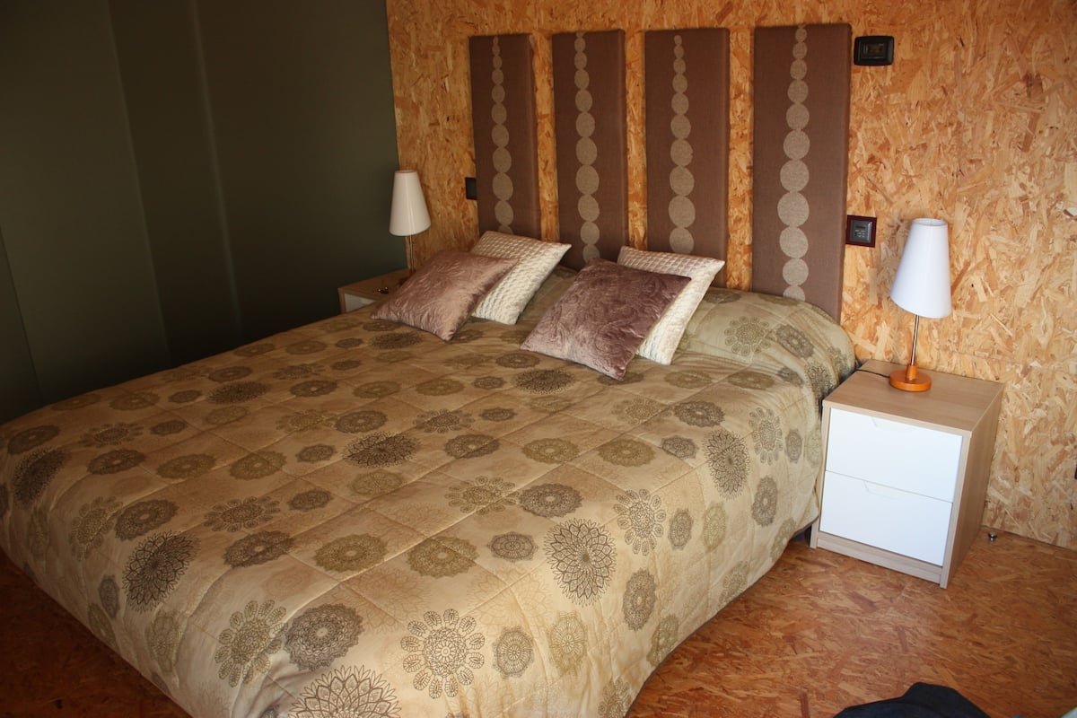 A neatly made bed with patterned bedding, a bedside table with a lamp, and a wall with a wooden panel design.