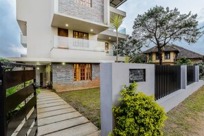 Une maison moderne à deux étages, dotée d’une façade en pierre, d’un balcon et d’une pelouse bien entretenue.