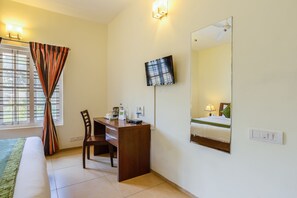 Une chambre d’hôtel comprenant un lit, un bureau, une chaise, un téléviseur fixé au mur et une fenêtre avec des rideaux.