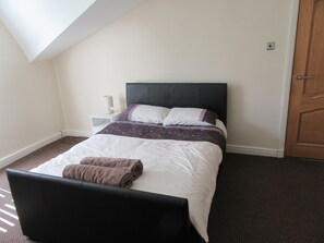 A neatly made bed with a headboard, a bedside table with a lamp, and a door to the right. - Aigburth Apartments - Sandringham (Liverpool)