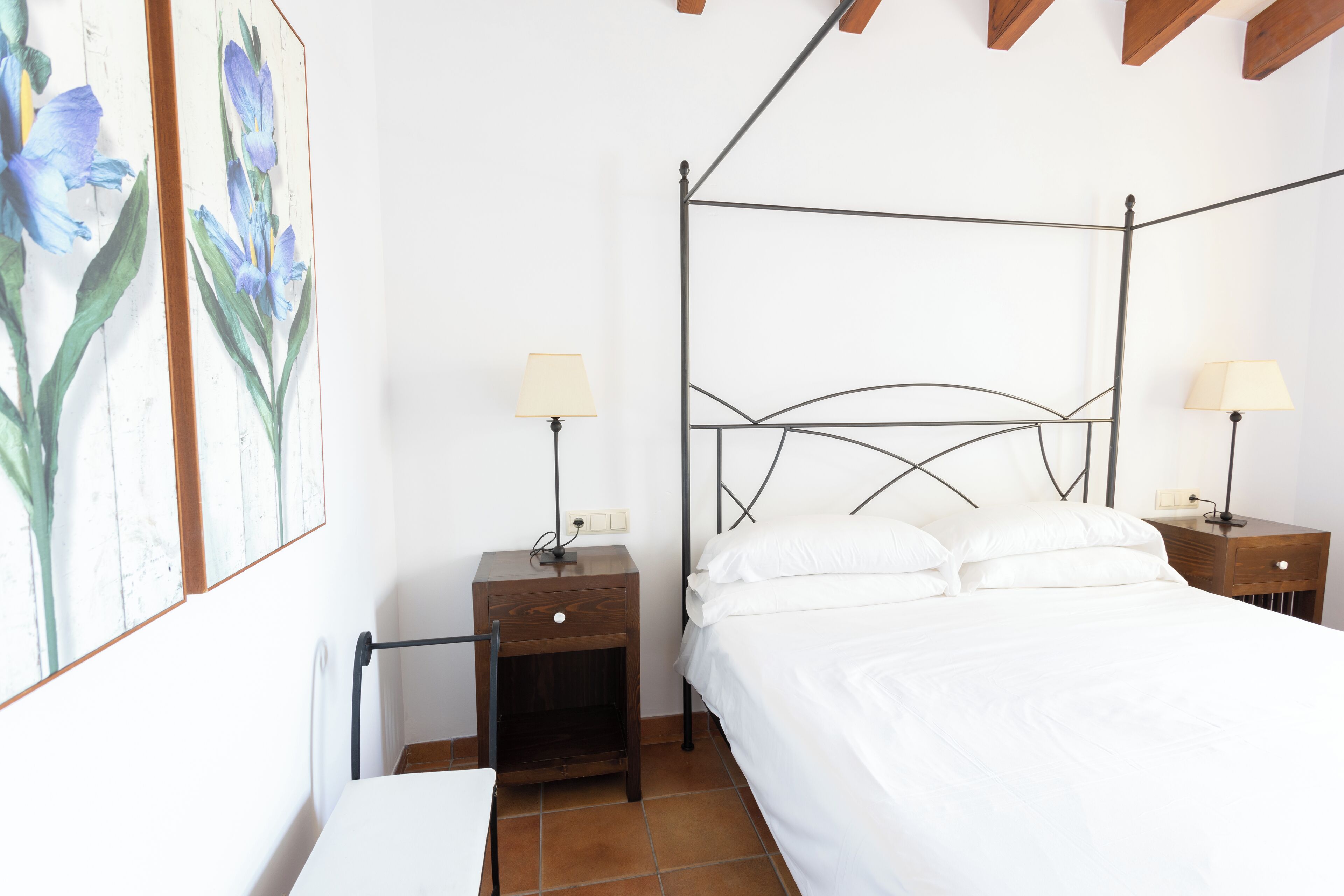 A bedroom with a metal bed frame, white bedding, two bedside tables with lamps, and a wall-mounted power outlet.