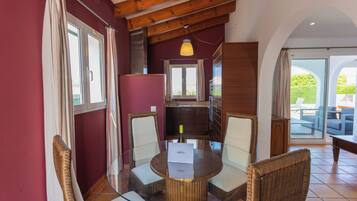 Un comedor con una mesa de vidrio rodeada de sillas de mimbre, techo de madera y vista al patio exterior.
