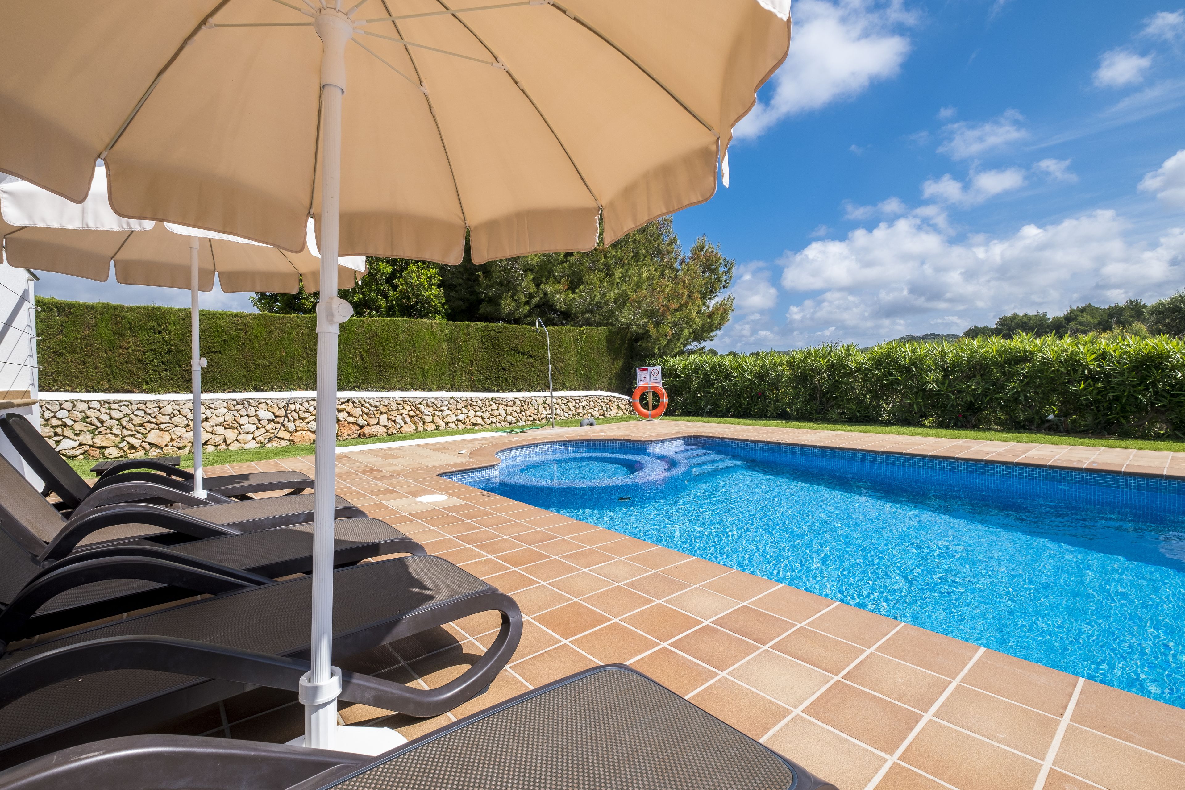 Una piscina con sillas de descanso y una sombrilla, rodeada por un muro de piedra y vegetación.