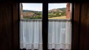 Una ventana con cortinas blancas, con vistas a un paisaje montañoso con vegetación y afloramientos rocosos.