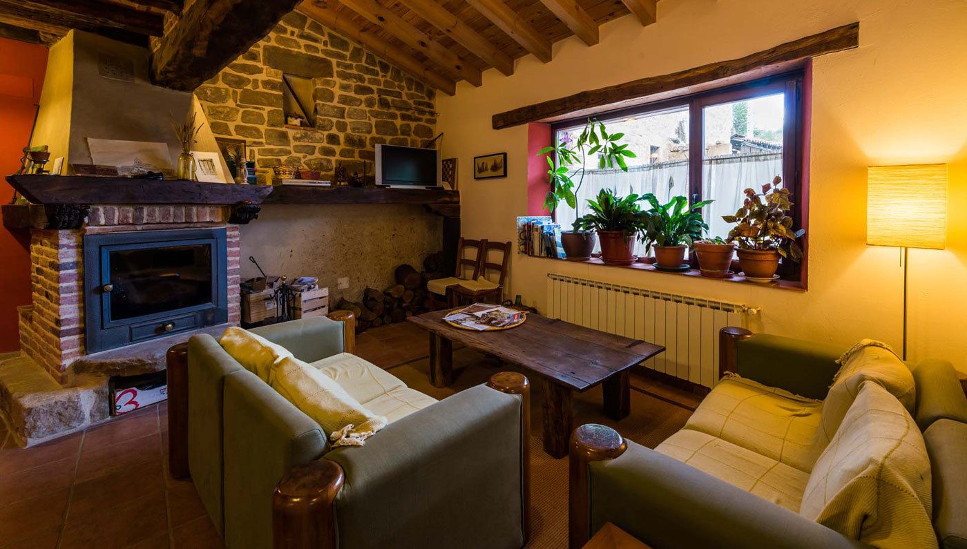 A cozy living room with a fireplace, comfortable seating, a table, and a window with plants.