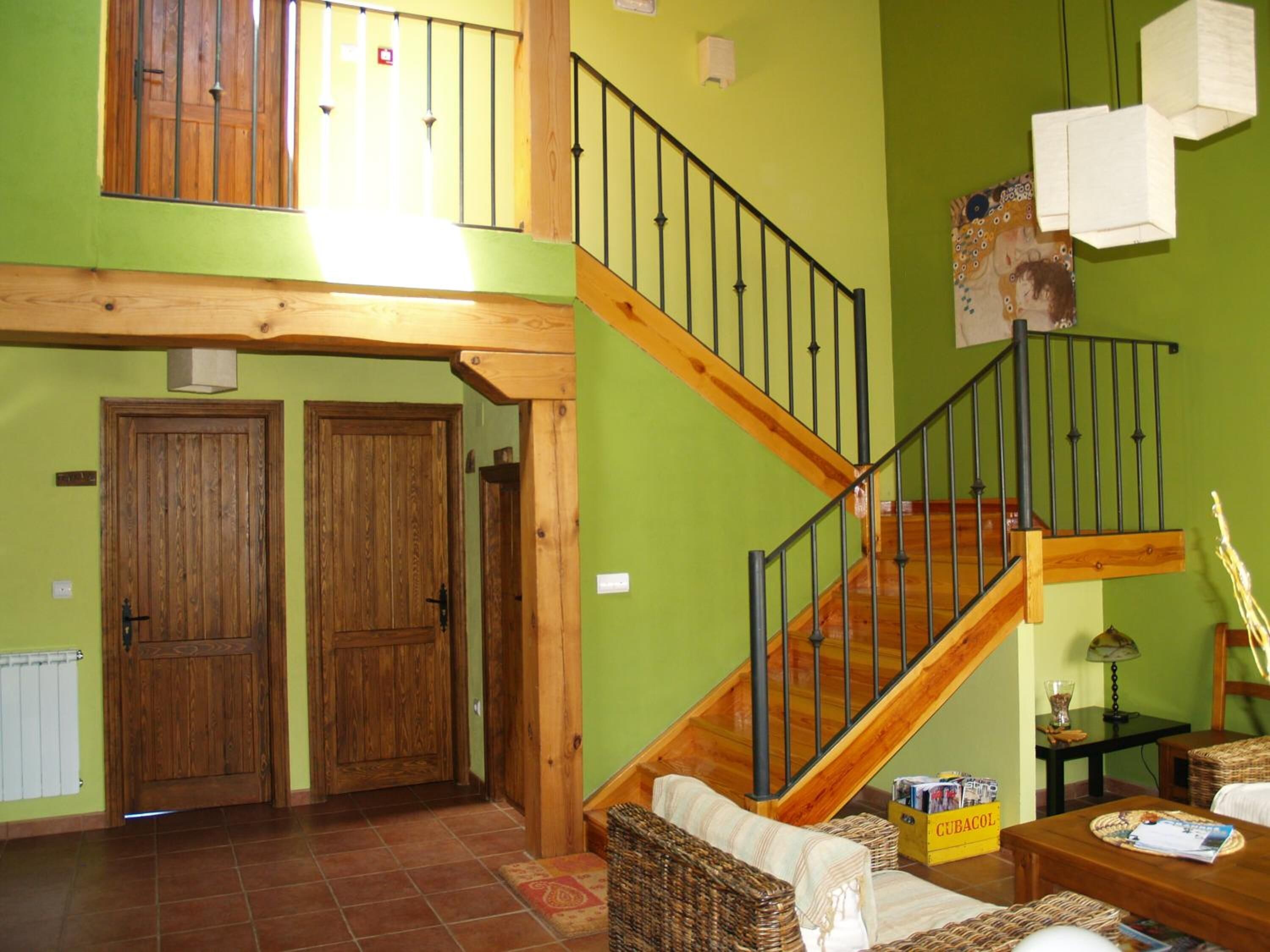 A spacious living area with a wooden staircase, two wooden doors, and a green wall.