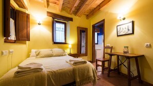 A room with a bed, a table, and a chair. There is a window with curtains, a wall-mounted lamp, and a framed picture. - Hotel Rural Piedra Abierta (San Cebrian de Muda)