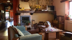 A cozy living room with a stone fireplace, wooden furniture, and a television mounted on the wall. - Hotel Rural Piedra Abierta (San Cebrian de Muda)
