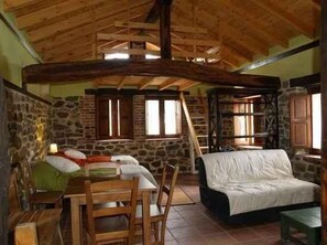 Ein rustikaler Raum mit Steinwand, Holzbalken, einem Bett, einem Tisch und einem Stuhl.