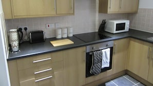 A kitchen with wooden cabinets, a black countertop, a toaster, a microwave, and a stove. - Aigburth Apartments - Ivanhoe (Liverpool)