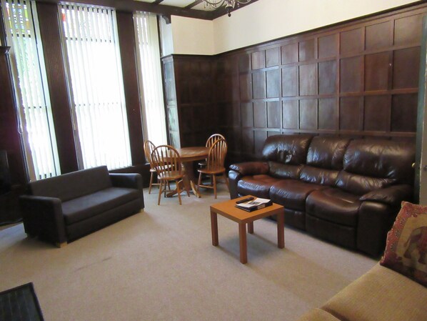 A living room with a dark brown leather sofa, a wooden coffee table, and a dining area with wooden chairs and a table.