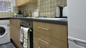 A kitchen with wooden cabinets, a washing machine, a kettle, and a toaster. - Aigburth Apartments - Ivanhoe (Liverpool)
