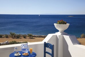 Une table avec une carafe, un verre et une assiette de nourriture, donnant sur une vue de la mer avec un voilier et une terre lointaine.