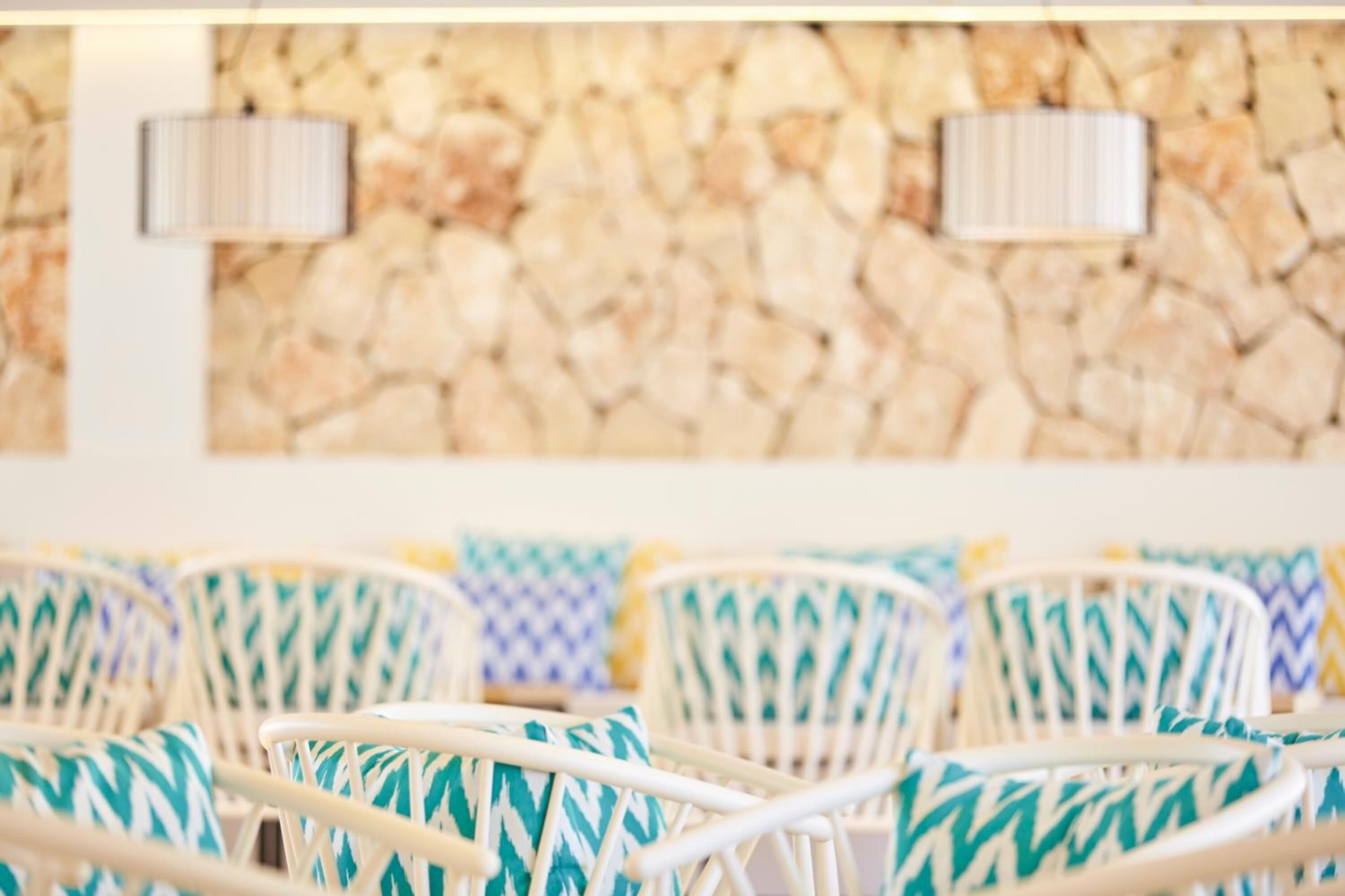 Wicker chairs with patterned cushions, a stone wall, and two wall-mounted lamps.