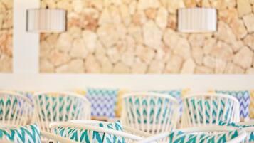 Wicker chairs with patterned cushions, a stone wall, and two wall-mounted lamps.