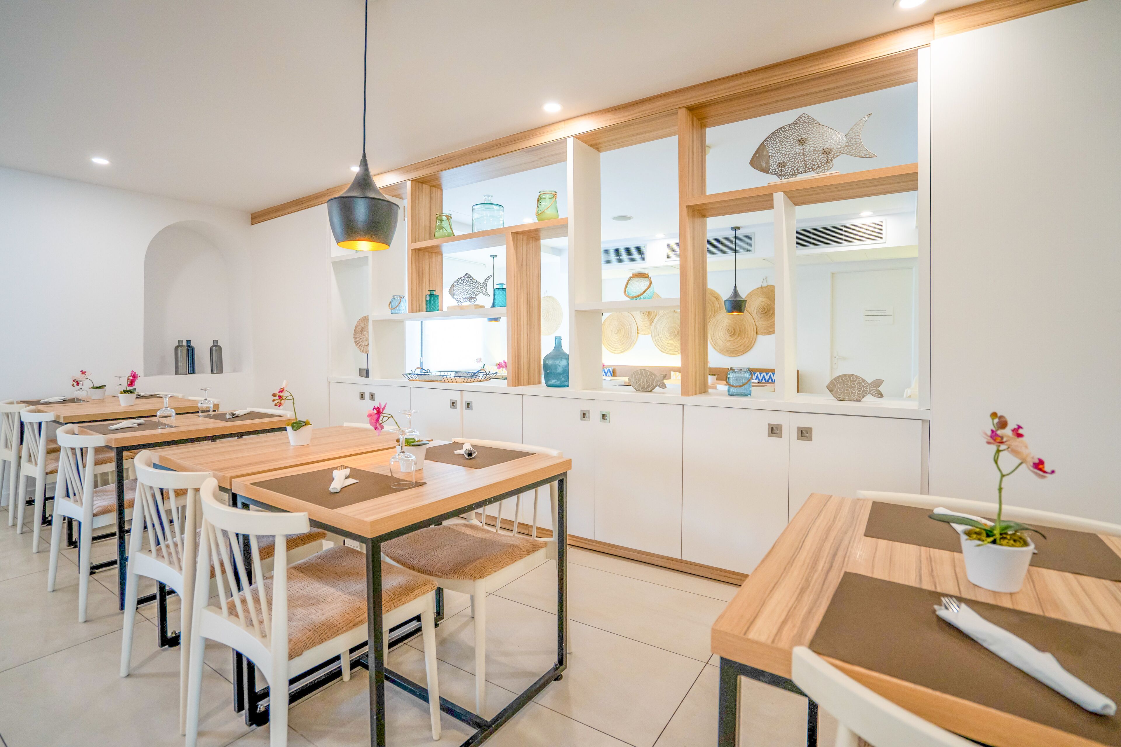 Un comedor moderno con mesas de madera y sillas blancas, que incluye una isla central con un lavamanos y una lámpara colgante.