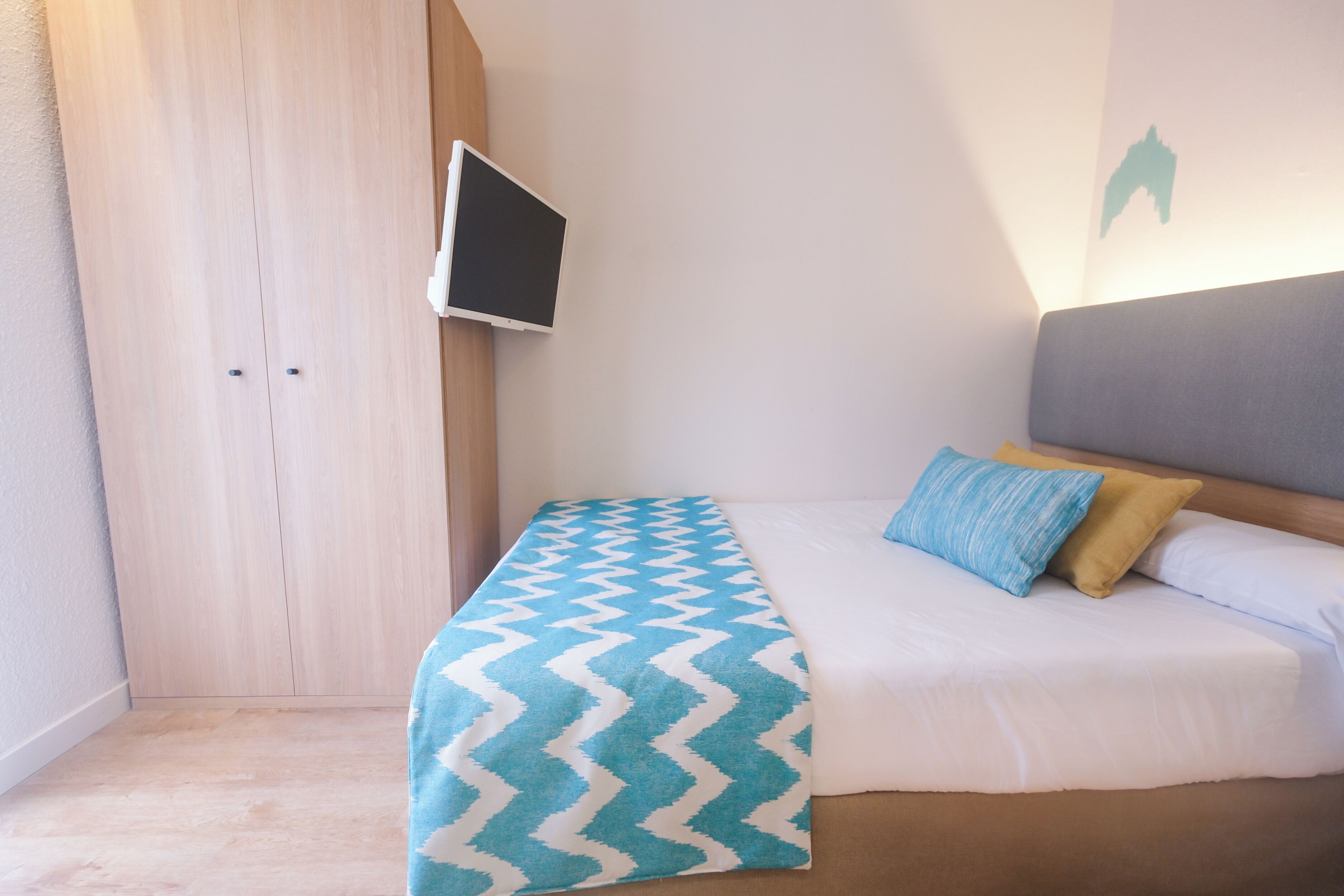 A bedroom with a bed, a TV mounted on the wall, and a wooden wardrobe.
