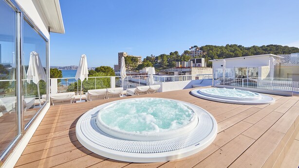 Una terraza en la azotea con dos jacuzzis, sillas de descanso y vistas al mar.