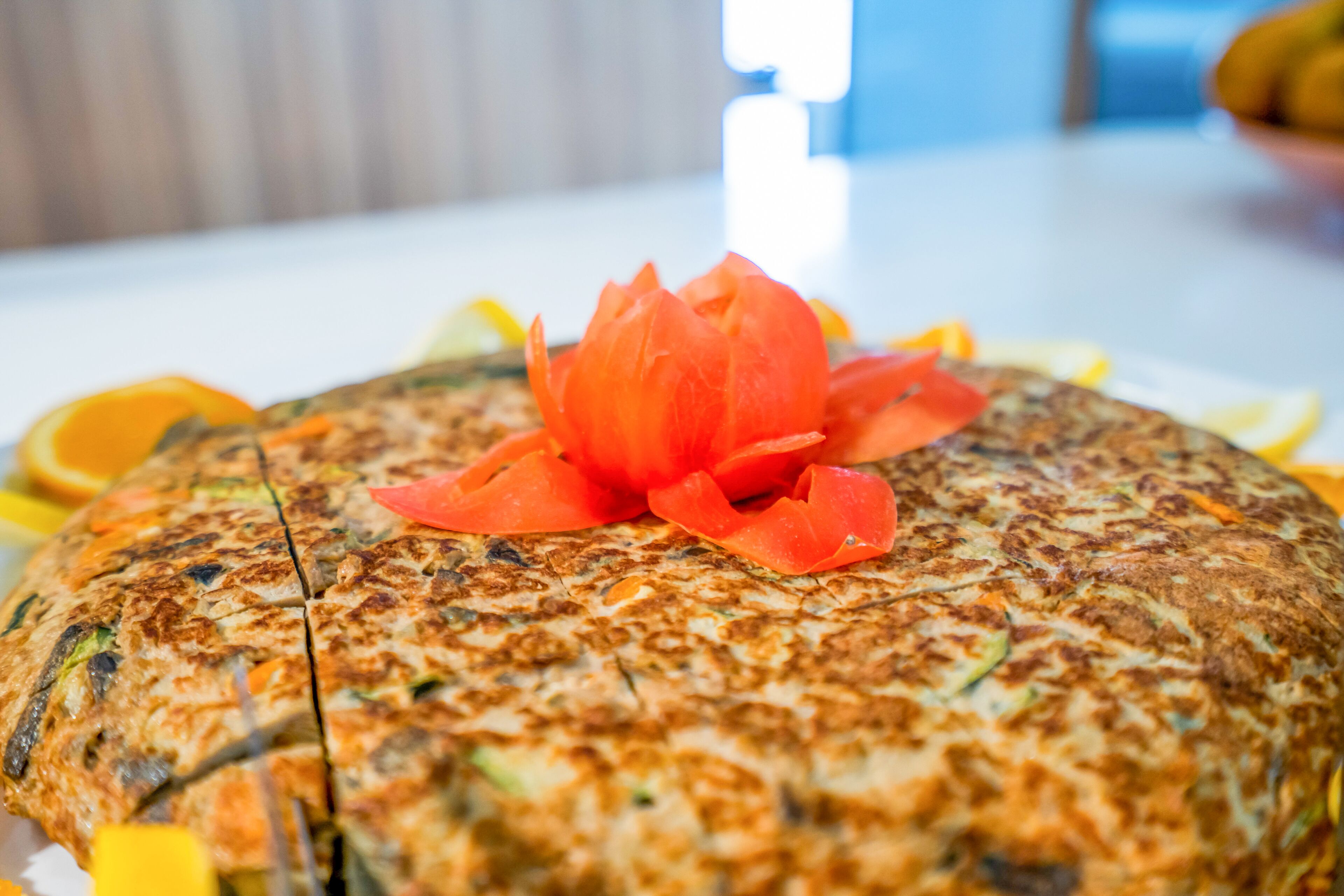 Un plato grande, redondo y dorado con una flor roja decorativa encima, rodeado de rodajas de naranja.