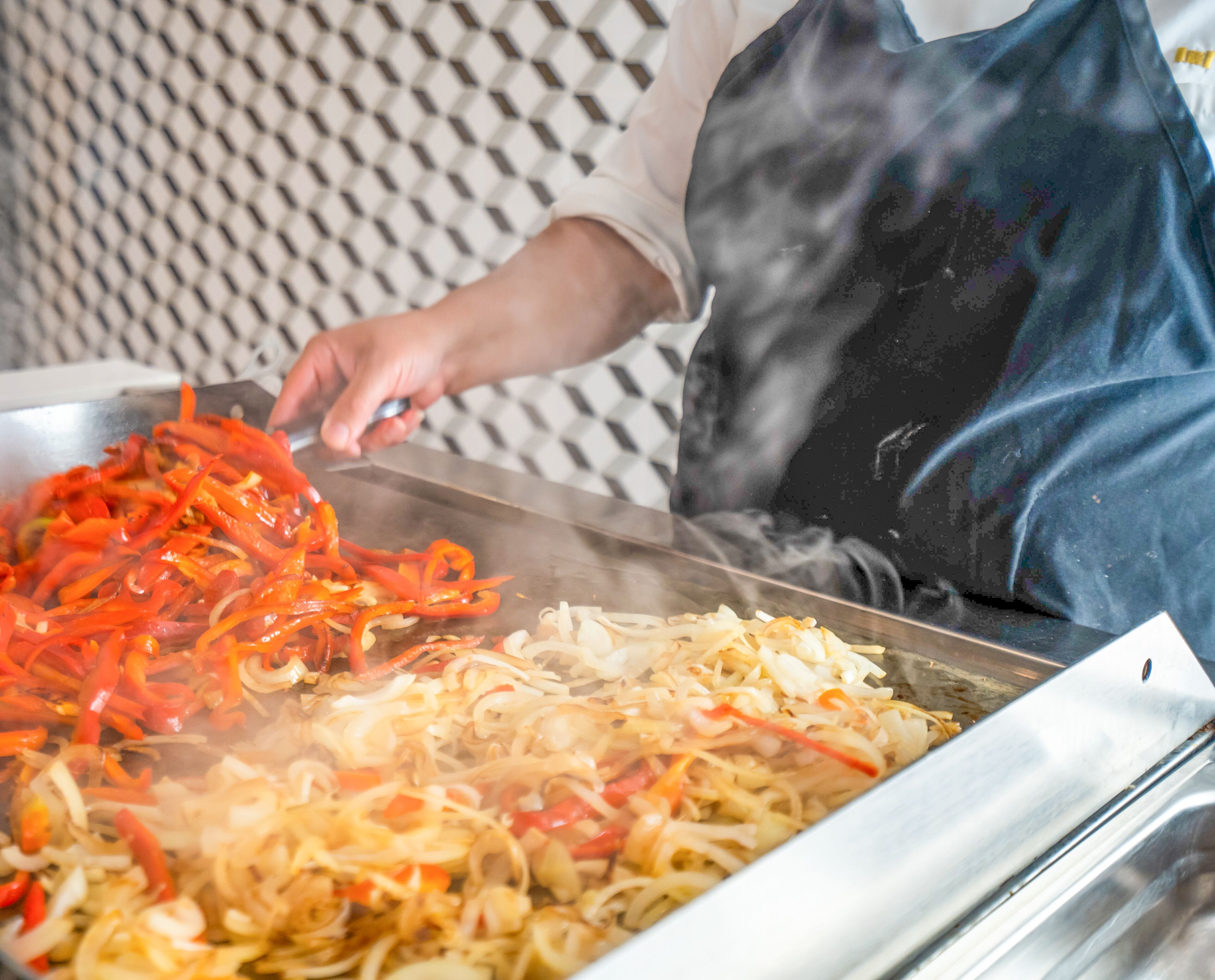 Une personne prépare des légumes sautés dans un grand plat à frire.