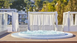 Un jacuzzi en una terraza de madera con sillas y un dosel blancos, con vistas a un paisaje montañoso.