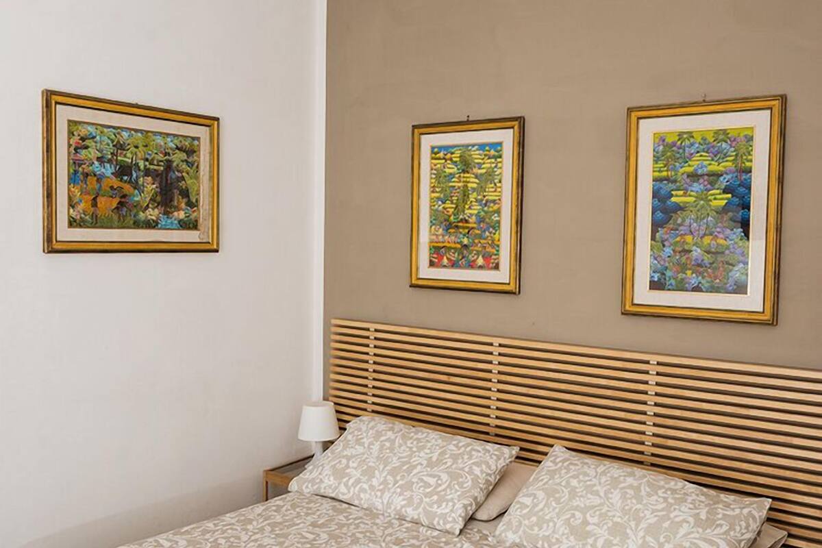 A bedroom with a bed, a nightstand, and three framed pictures on the wall.