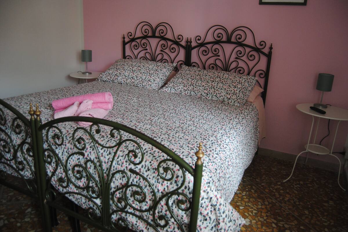 A bed with a metal frame and floral bedding, two bedside tables, and a pink wall.