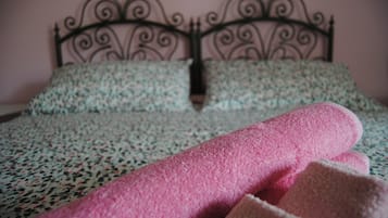 A bed with a patterned bedspread and pillows, and rolled towels in pink and beige.
