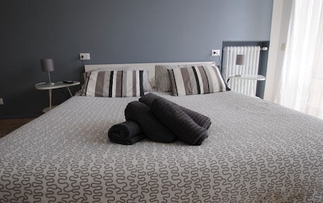 A neatly made bed with a patterned bedspread, two bedside tables with lamps, and a window with curtains.