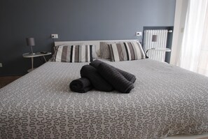A neatly made bed with a patterned bedspread, two bedside tables with lamps, and a window with curtains. - Pisaland (Pisa)