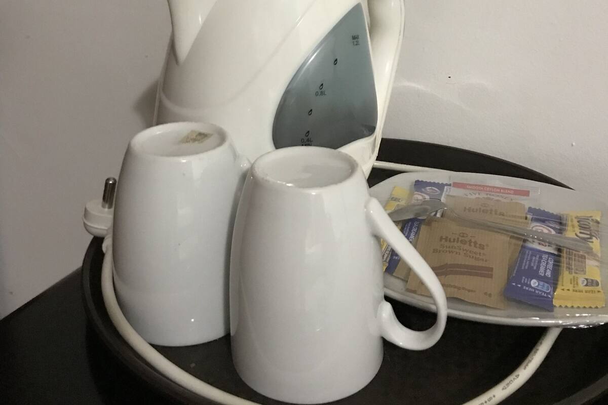A white electric kettle with two white cups on a tray.