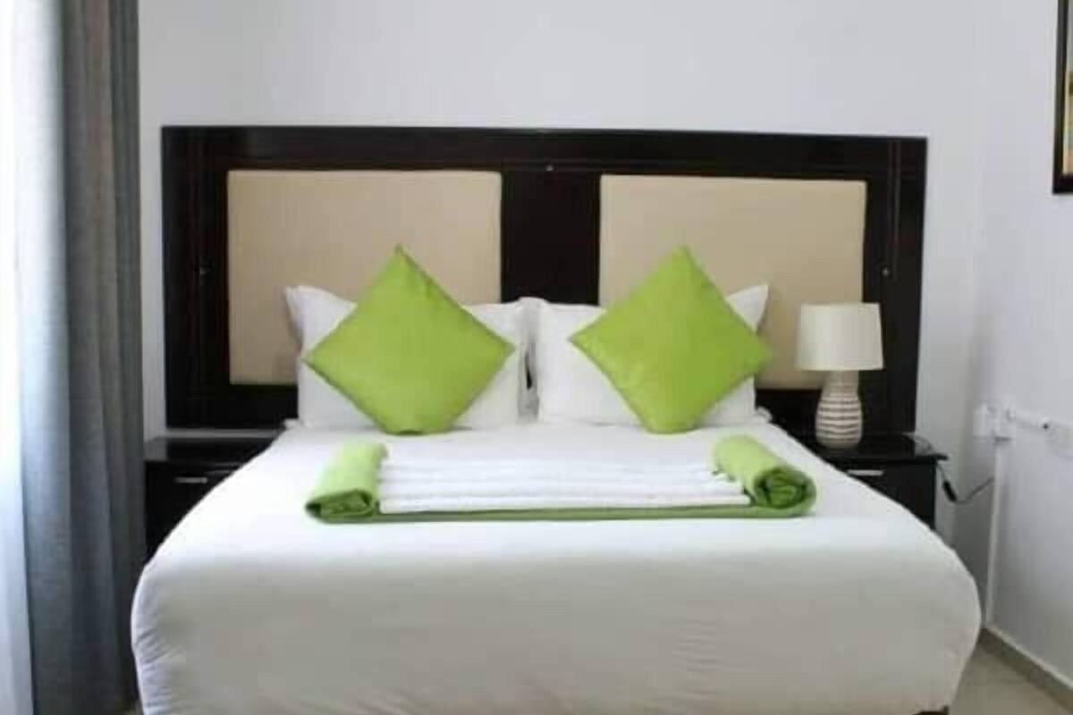 A neatly made bed with white bedding and green pillows, a bedside table with a lamp, and a grey striped rug.