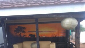 Zona d'estar a l'aire lliure coberta, amb un sofà beix, una tanca de fusta i un mural d'un capvespre.