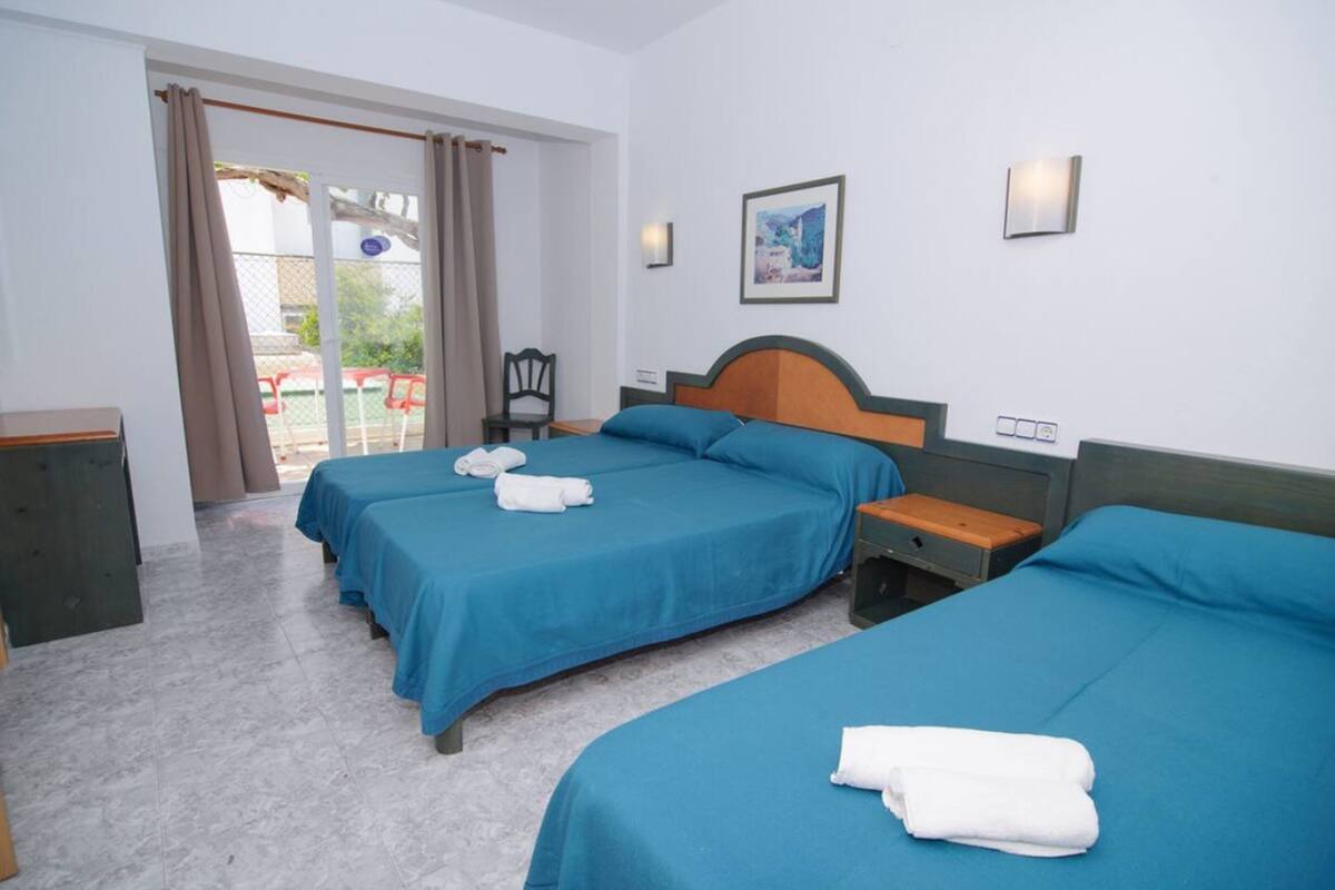 Ein Hotelzimmer mit zwei Betten, einem Sessel, einem Schreibtisch und einem fensterbepflanzten Fenster.