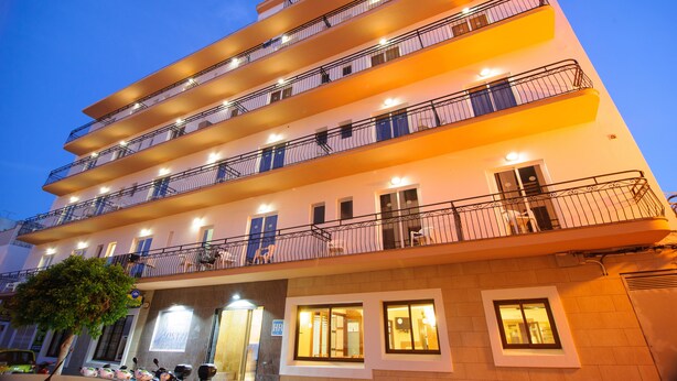A multi-story hotel with balconies, a visible entrance, and a tree in front.
