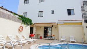 A hotel with a swimming pool, white walls, and multiple windows.