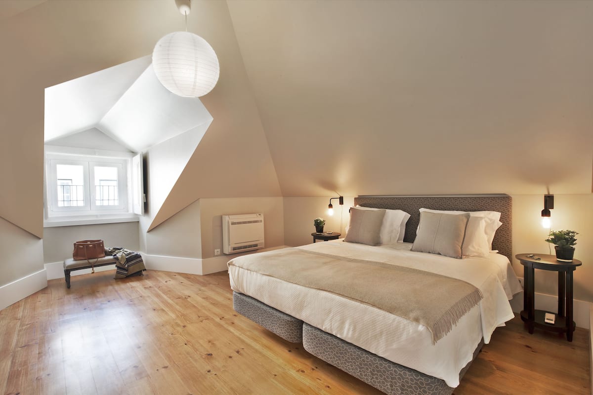 A bedroom with a large bed, wooden flooring, a sloped ceiling, and a window.