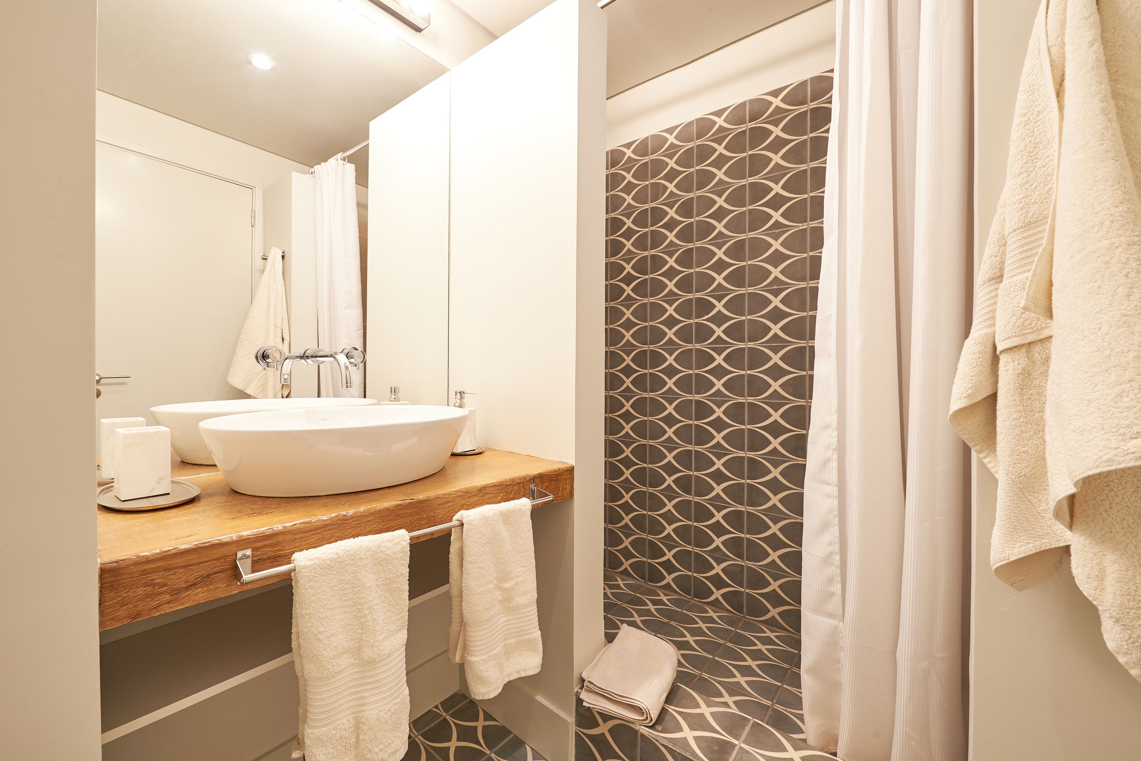Un baño moderno con un tocador de madera, un lavamanos grande y una ducha con azulejos estampados.