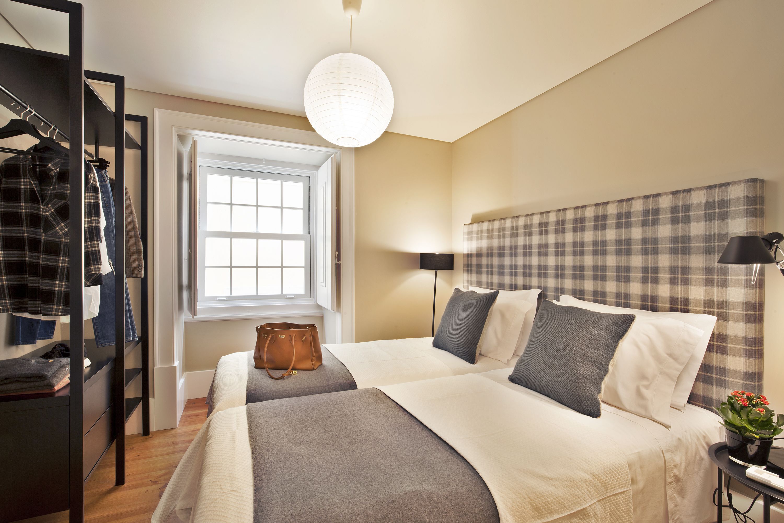 A hotel room with two beds, a wardrobe, a window, a lamp, and a plant.