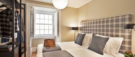 A hotel room with two beds, a wardrobe, a window, a lamp, and a plant.