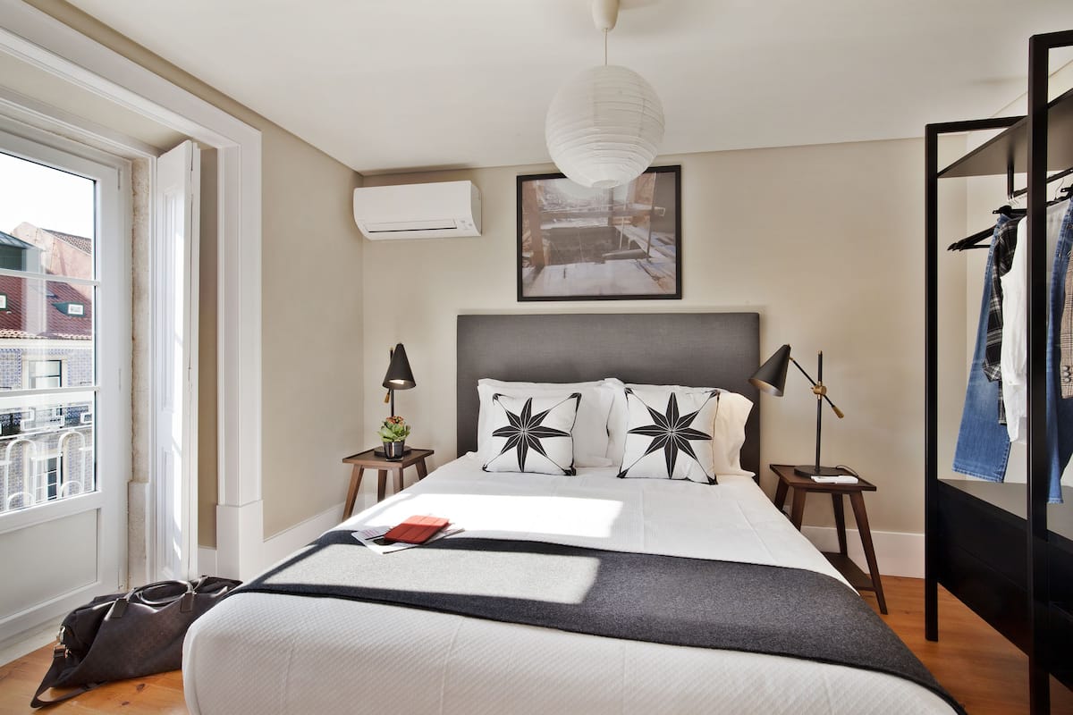 A neatly arranged bedroom with a large bed, bedside tables, a hanging light, and a view through a window.