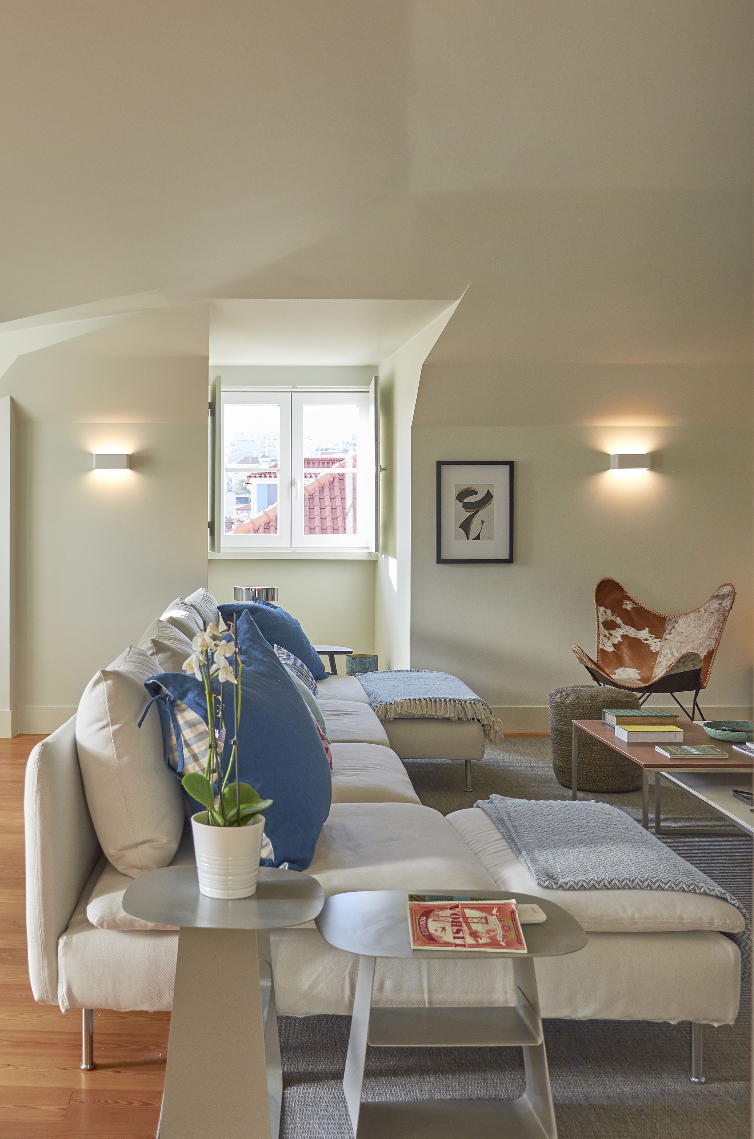 En moderne stue med sofa, sofabord, stol og et vindue med udsigt til bygninger.