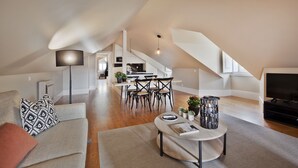 A spacious living area with a high ceiling, a dining table with chairs, a sofa, a coffee table, and a TV. - Lisbon Five Stars Apartments - Bica 246 (Lisbon)