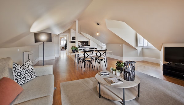 A spacious living area with a high ceiling, a dining table with chairs, a sofa, a coffee table, and a TV.