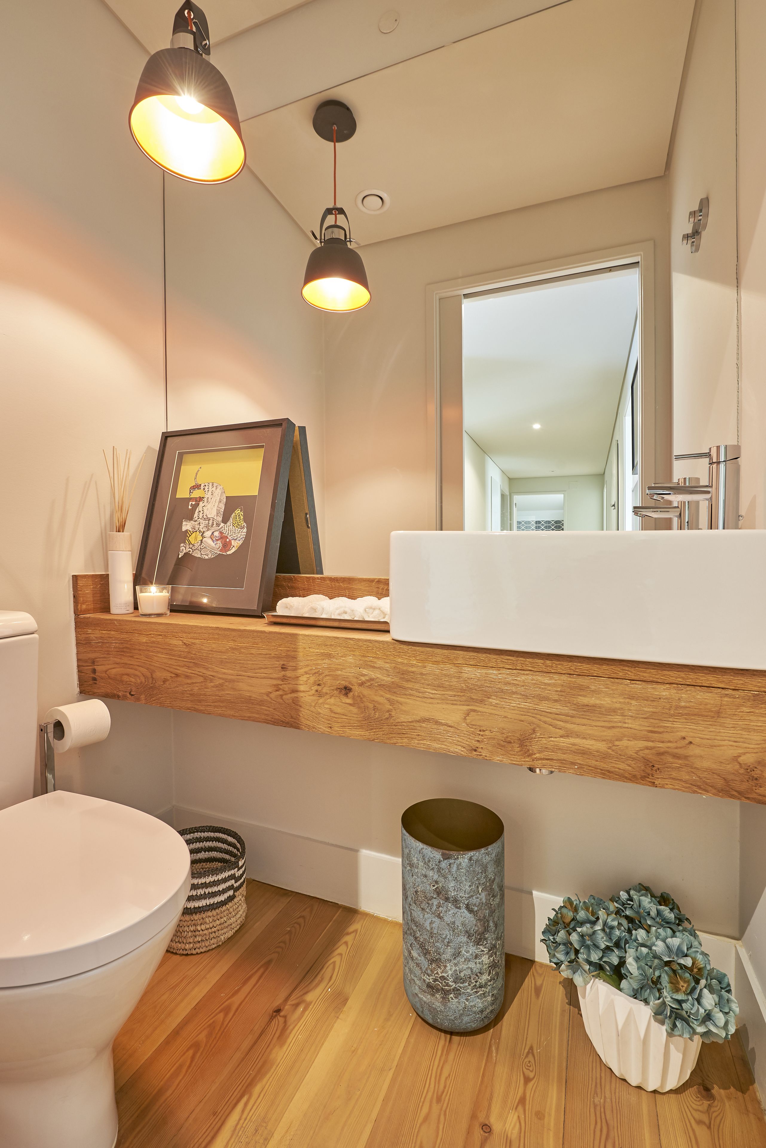 Un baño moderno con un tocador de madera, un espejo grande y un cuadro enmarcado sobre el lavabo.