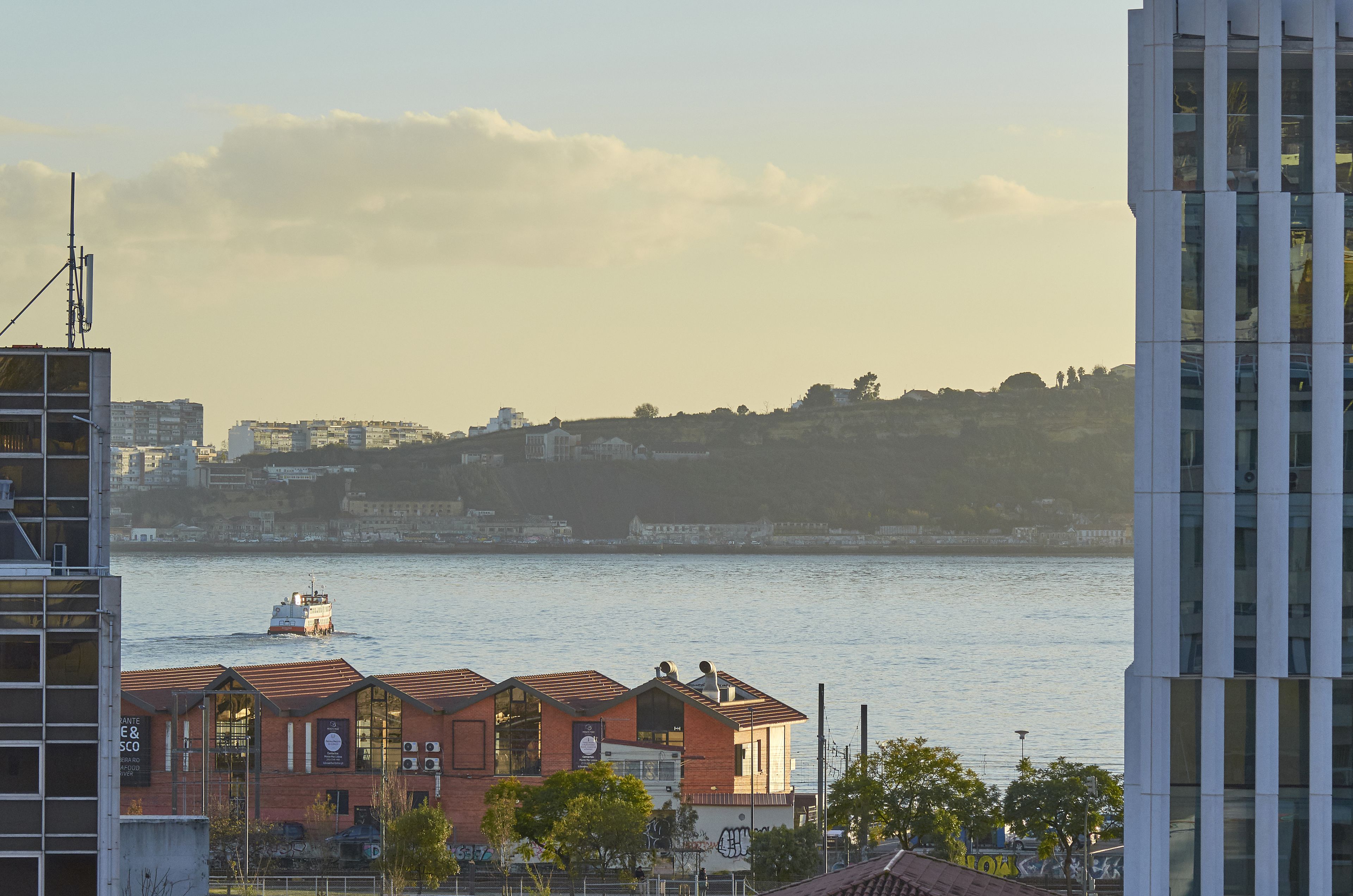 A waterfront view with buildings, a boat, and a hill in the background.