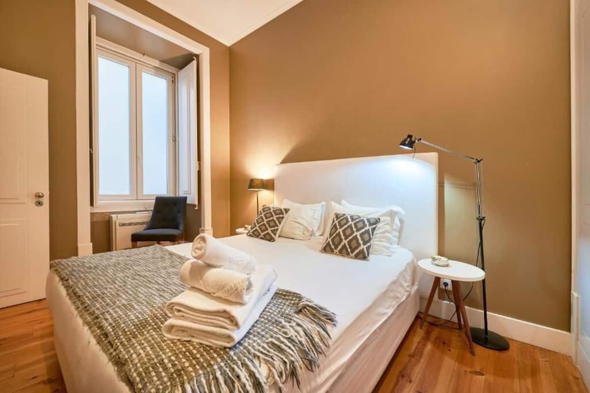 A bedroom with a bed, bedside lamp, and a window.