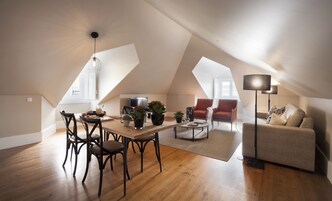 Um amplo apartamento loft com área de jantar, sala de estar com sofá e poltronas, e uma grande janela que oferece muita luz natural.