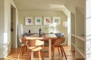 A modern dining area with a wooden table, four chairs, a wine bottle, and a coffee machine. There are framed artworks on the wall and a lamp on the side. - Lisbon Five Stars Apartments - Bica 246 (Lisbon)